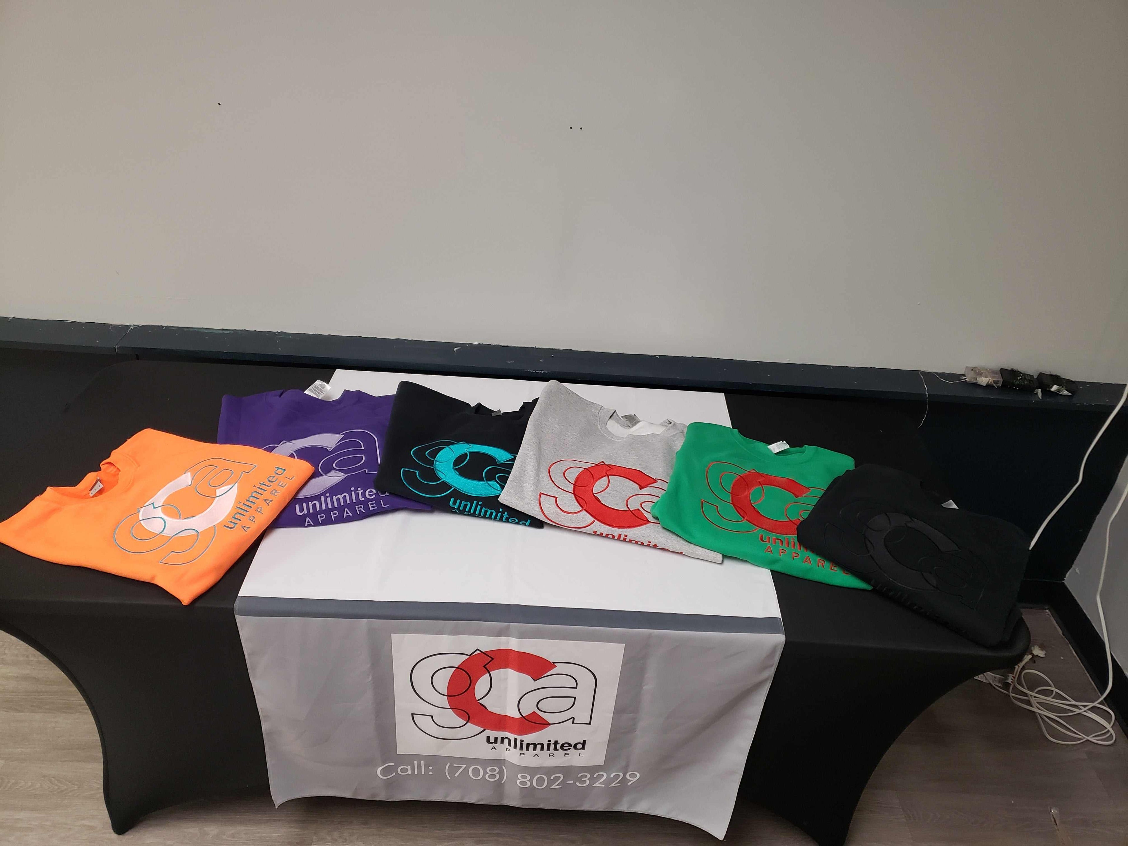 Custom sweatshirts displayed on a table, featuring various colors and designs by GCA Unlimited.