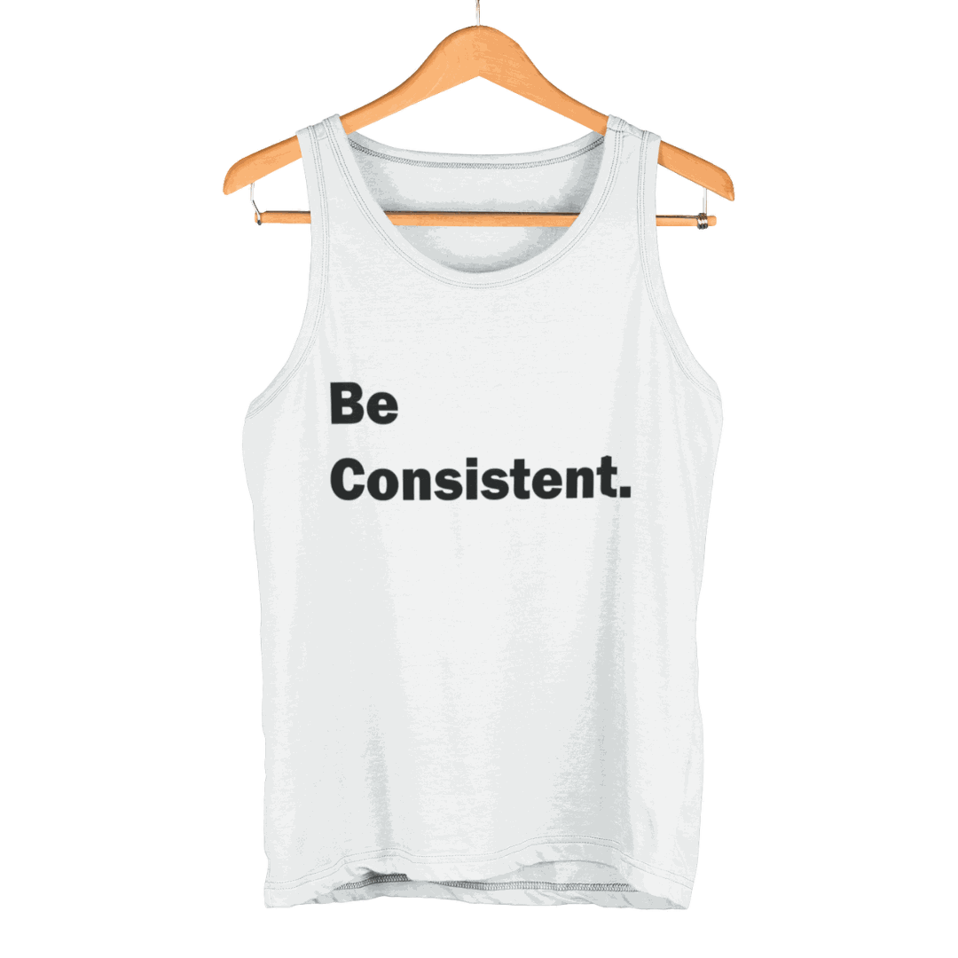 White Be Consistent Tank Top with bold black text hanging on wooden hanger